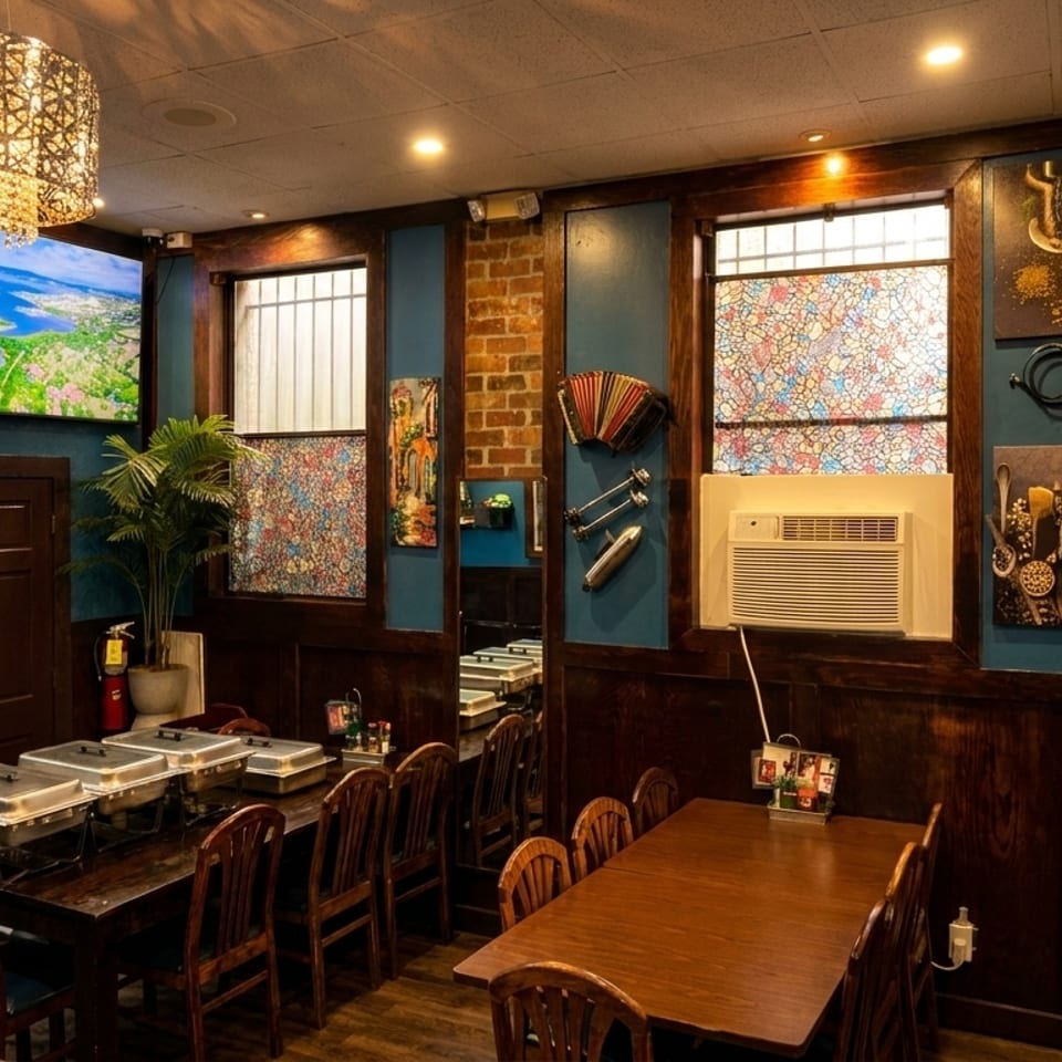 Restaurant interior with wooden tables, blue walls, a large TV, and decorative windows.