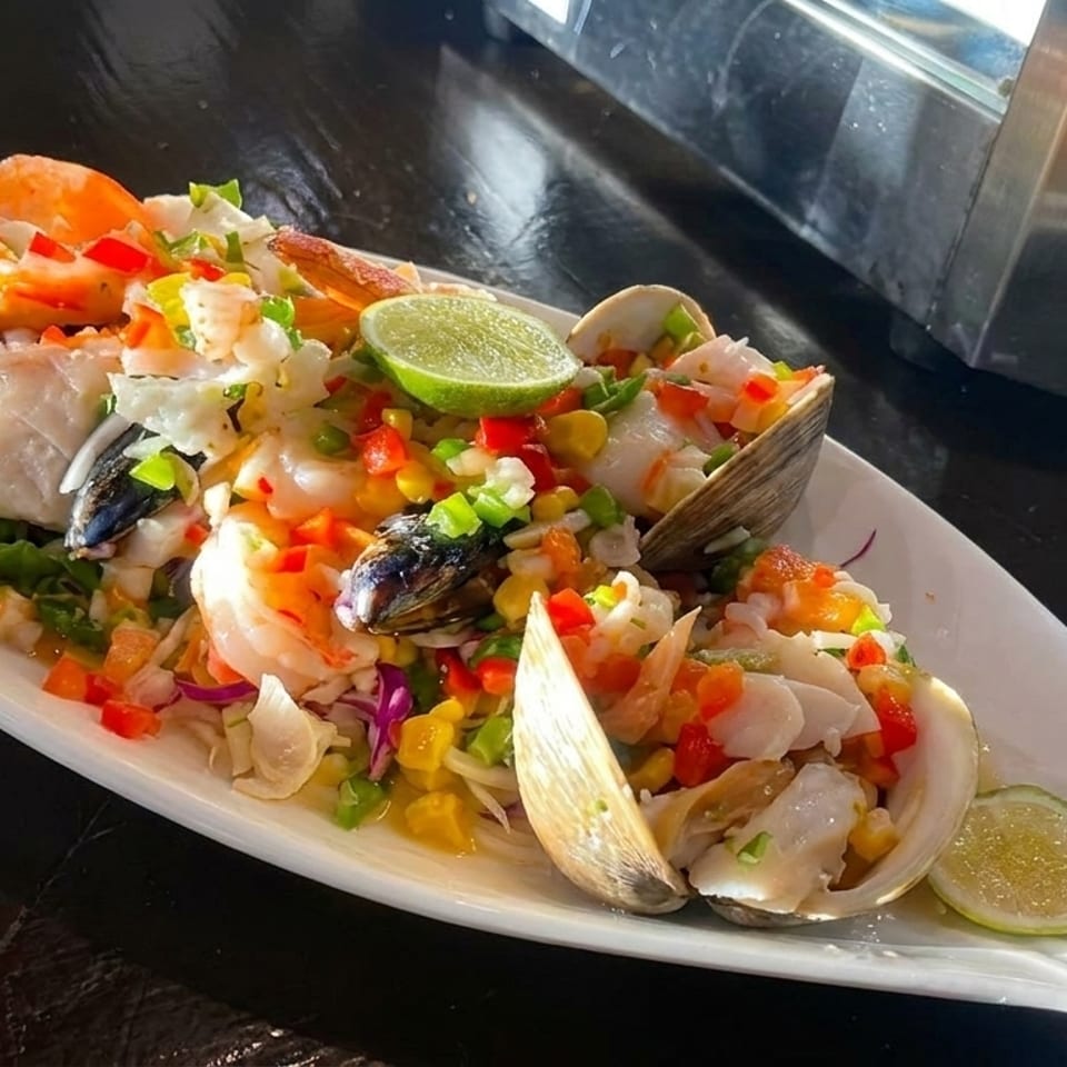 Seafood ceviche with shrimp, clams, mussels, fish, corn, and peppers on a fish-shaped platter.