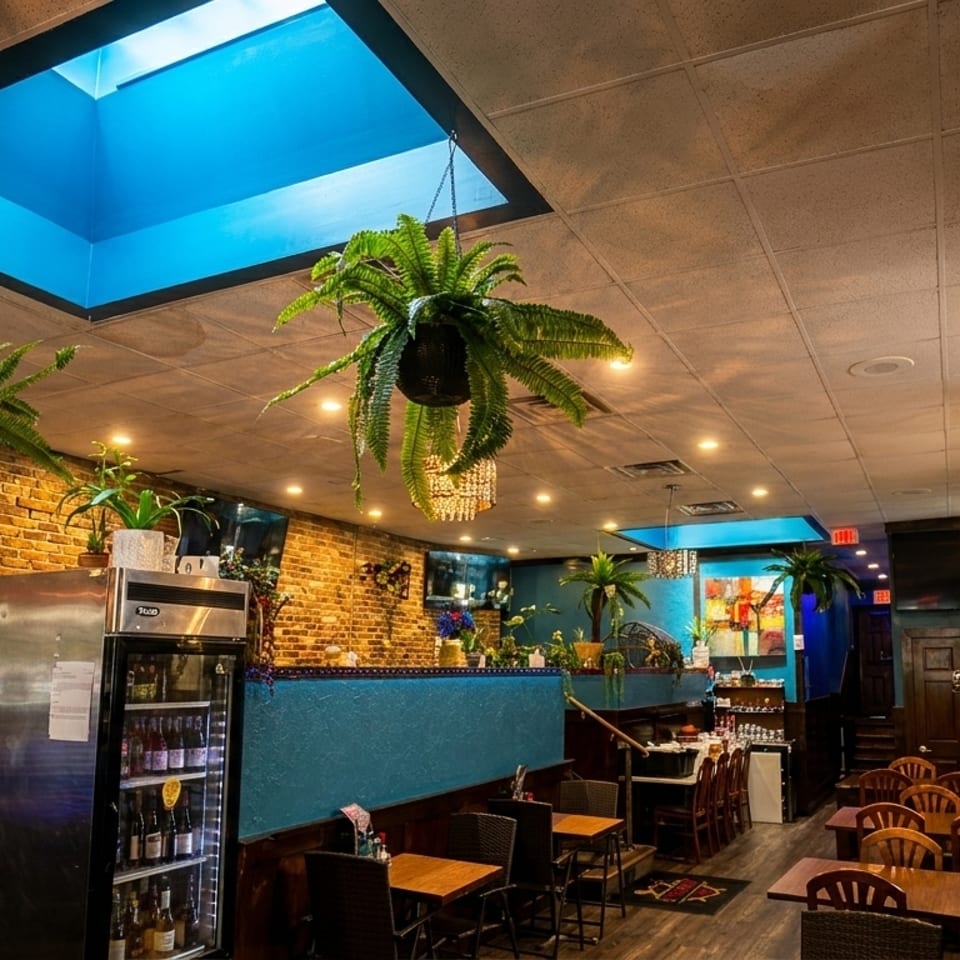 Restaurant interior with brick walls, blue accents, hanging plants, skylights, and wooden tables.