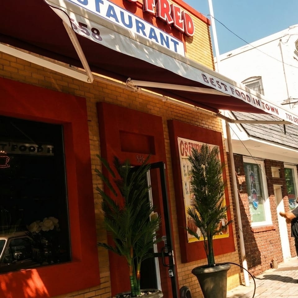 Exterior of a brick restaurant with red awnings and trim, a man stands on the sidewalk.