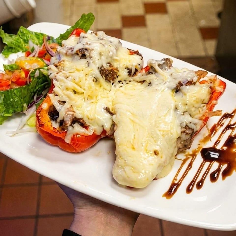 Two cheese-covered stuffed red bell peppers with a side salad on a white plate.